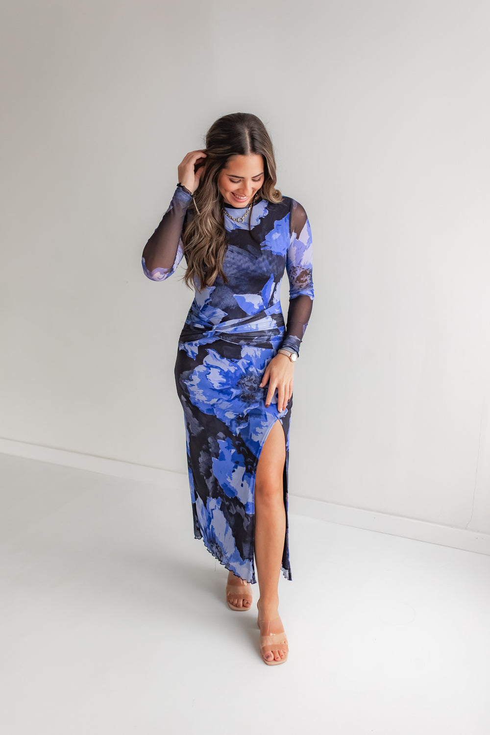 Woman wearing a blue floral mesh dress with a slit in the front with a pair of heels. 