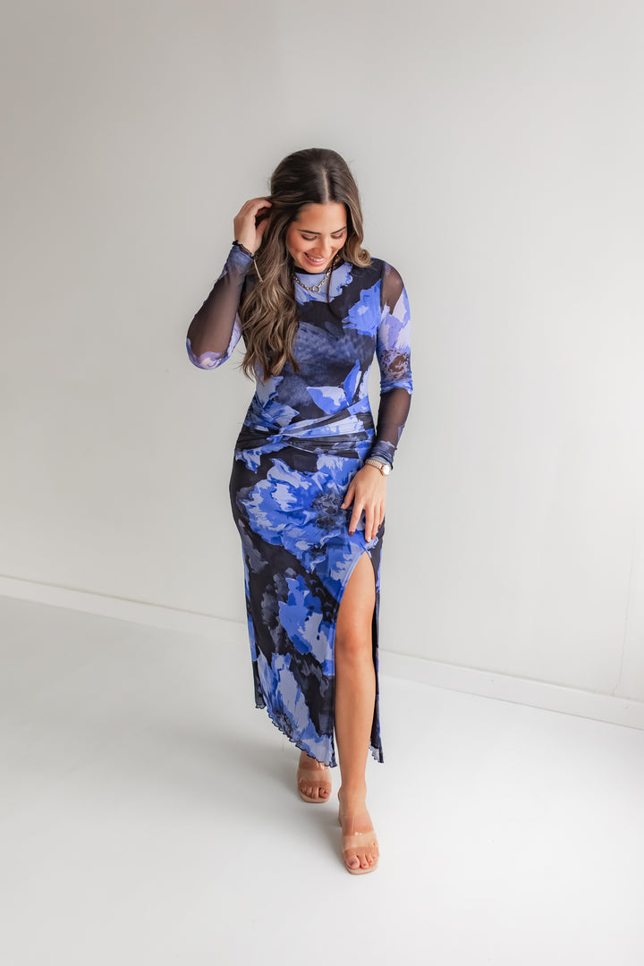 Woman wearing a blue floral mesh dress with a slit in the front with a pair of heels. 
