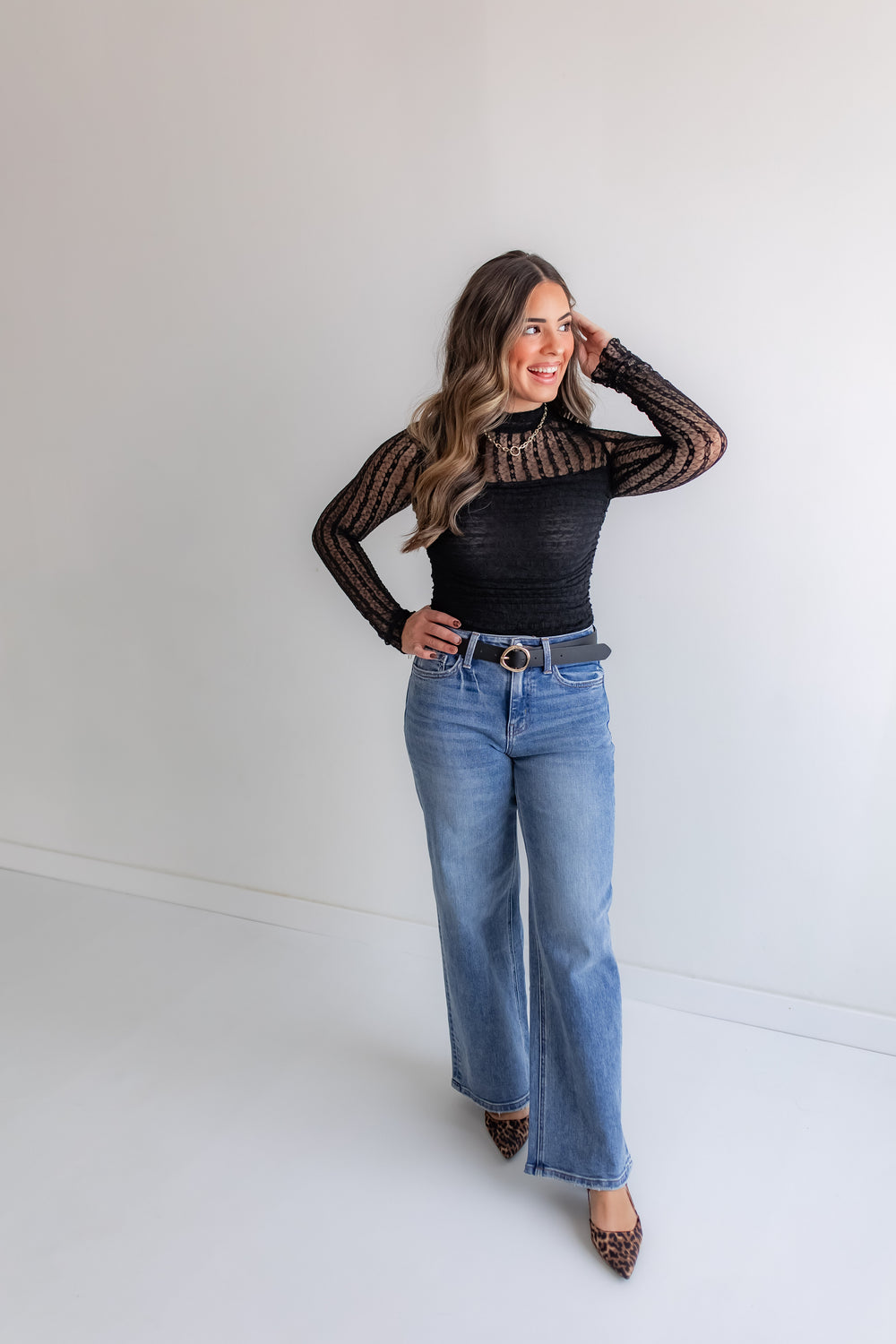 Woman wearing a black lace bodysuit with jeans and leopard heels. 