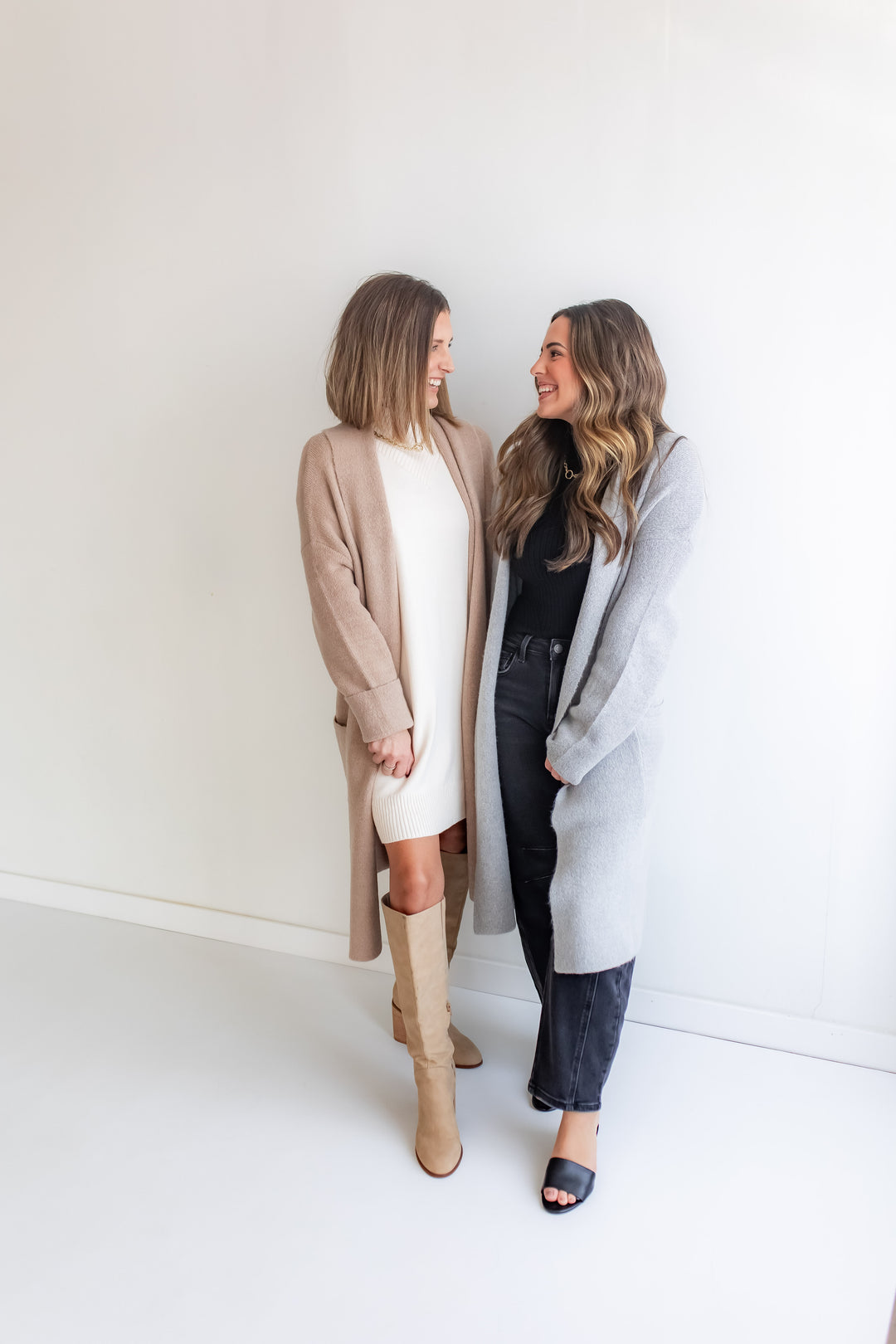 Two women standing side by side wearing long cardigans against a white background