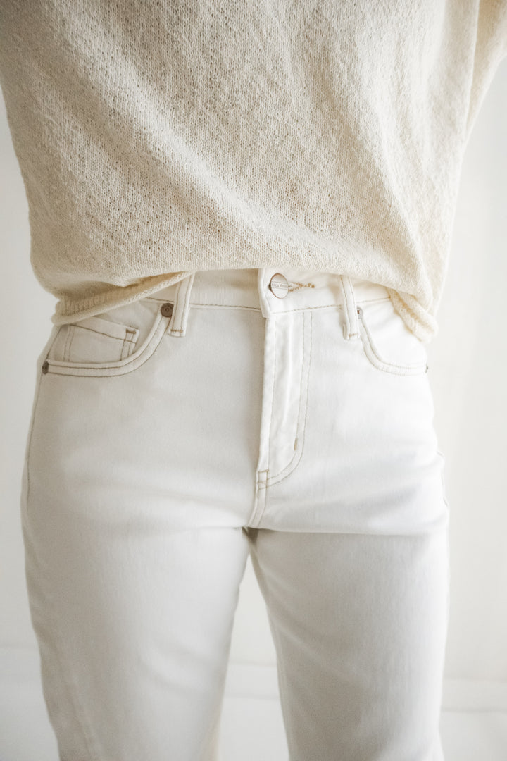 Person wearing a cream sweater and light-colored pants against a plain background