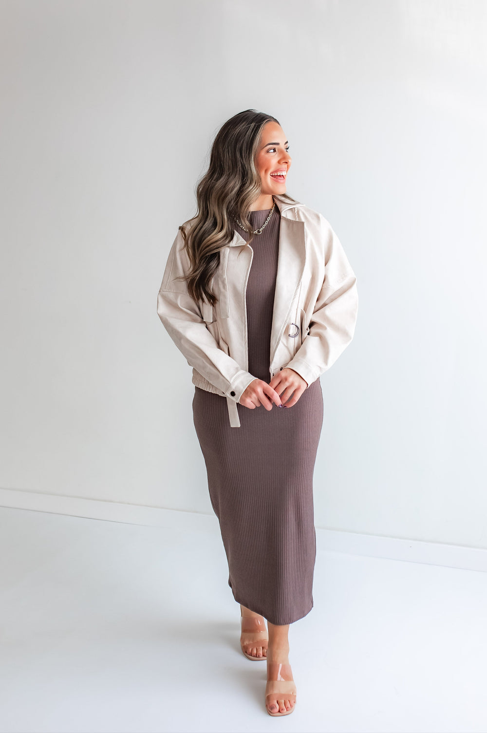 Woman wearing a leather jacket over a brown dress against a white background