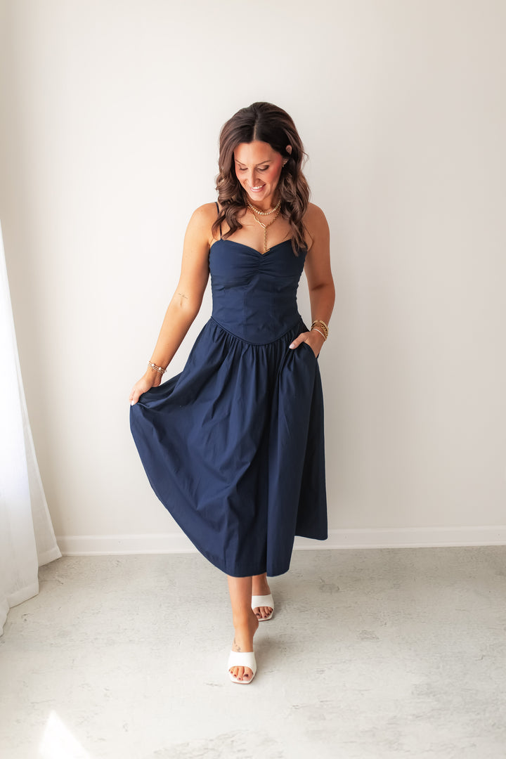 Navy midi dress with structured bodice and flowy skirt with pockets styled with sandals