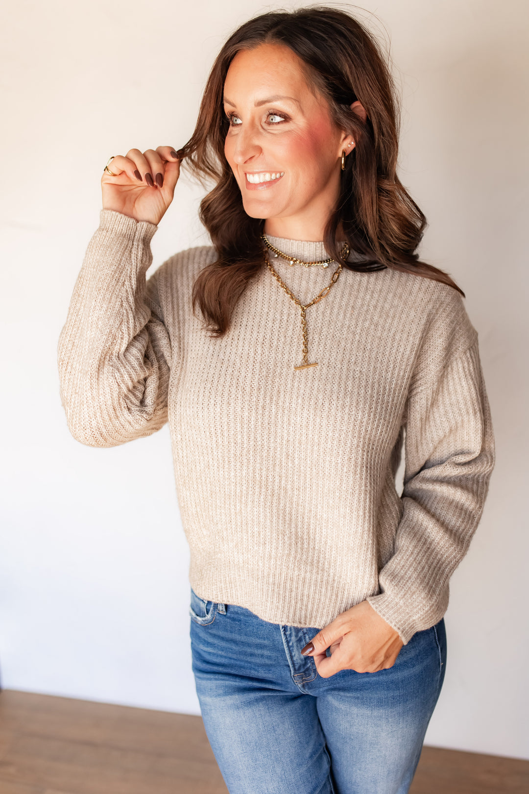Woman smiling in oatmeal ribbed mock neck sweater with layered gold necklaces