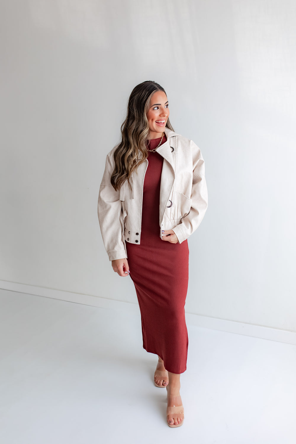 Woman wearing an ivory leather jacket over a rust fitted dress with heels. 