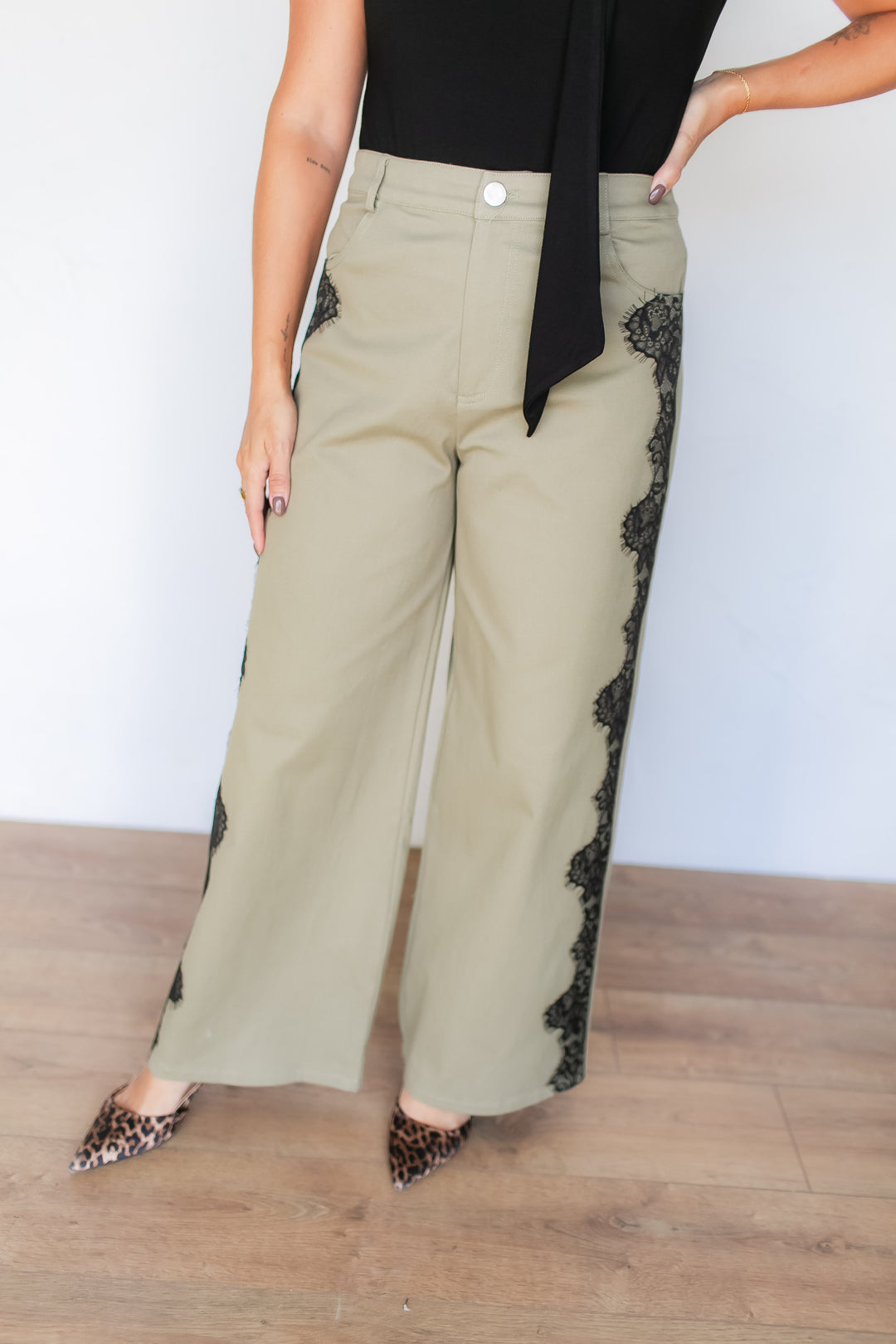 Woman wearing sage green wide leg pants with black lace appliqué detail, styled with a black top