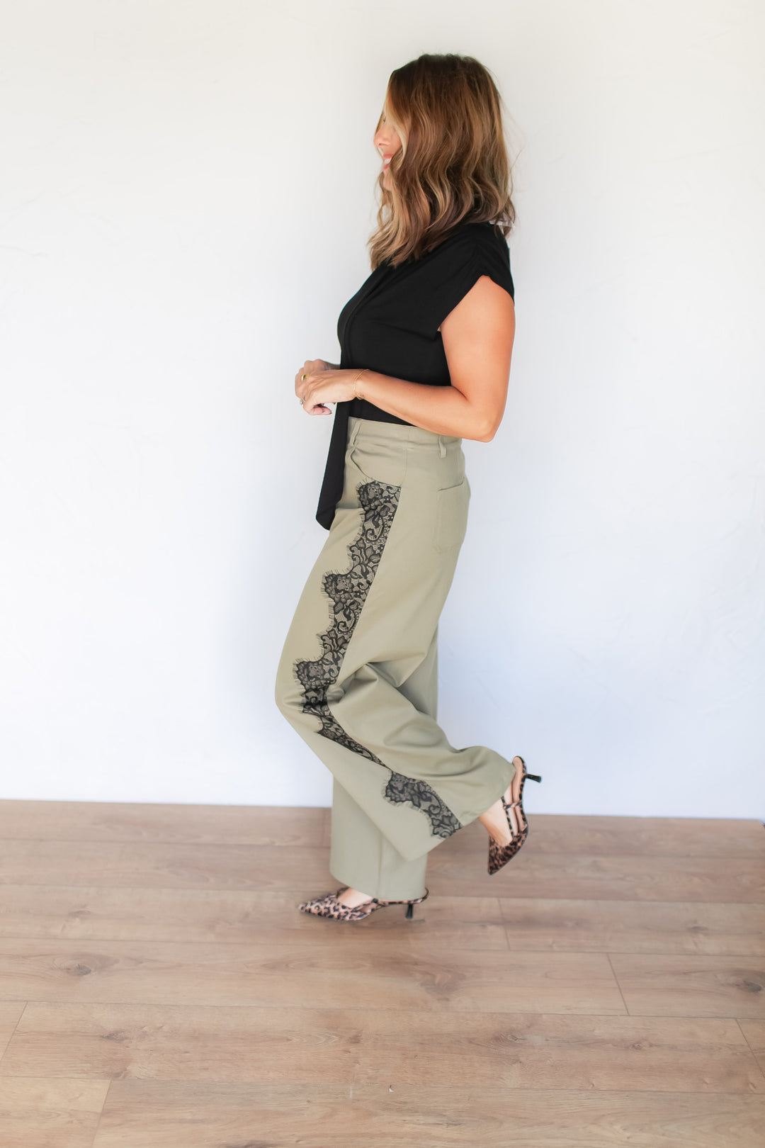 Side view of black floral lace appliqué on sage green trousers styled with black top