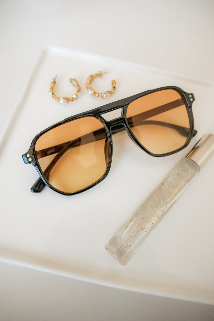 Skye sunglasses with a yellow lens with gold earrings. 