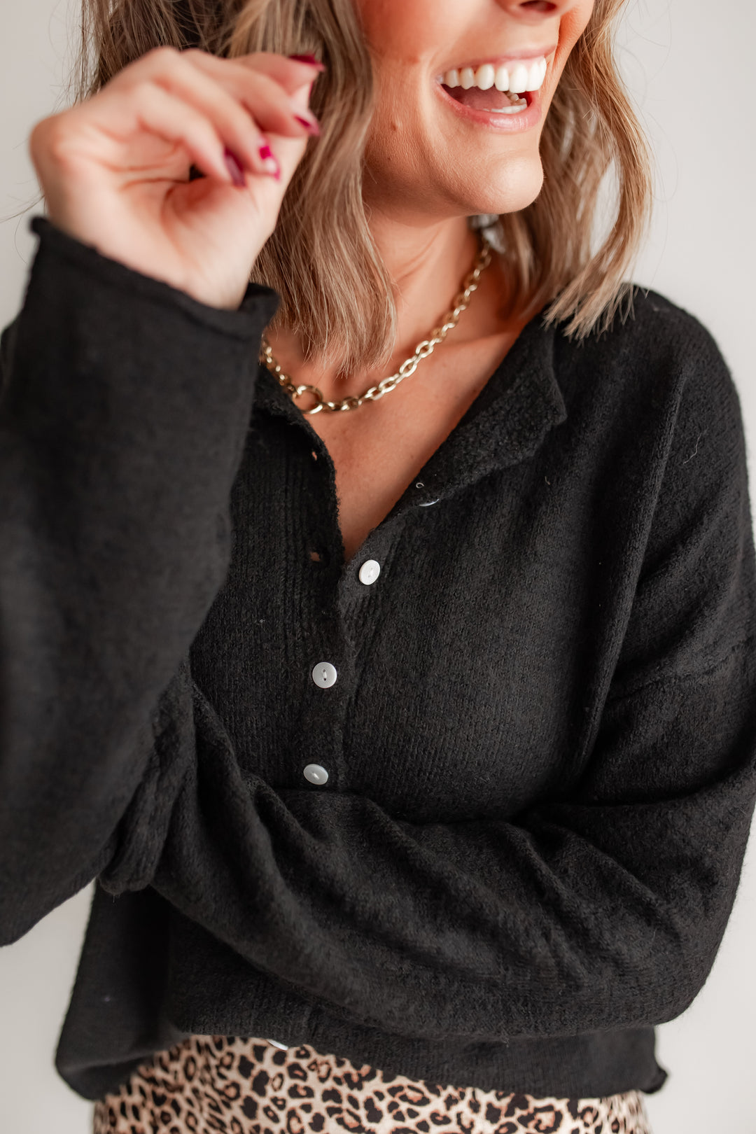 Close up of a woman wearing a black long sleeve cardigan and leopard bottoms. 