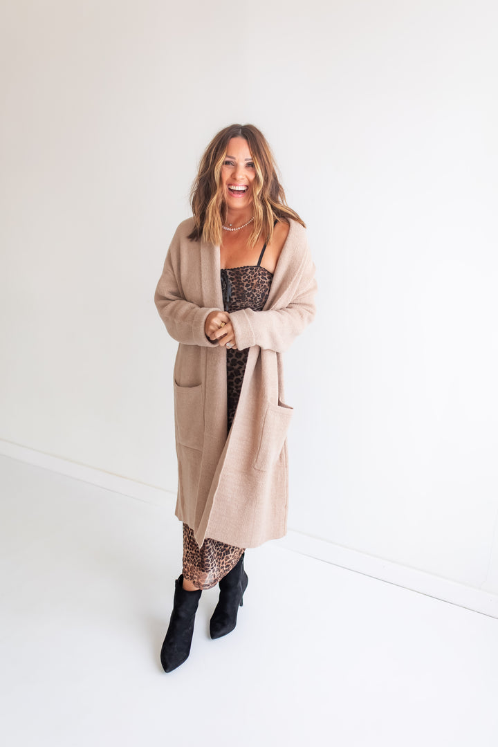 Woman wearing a beige cardigan over a leopard dress on a white background