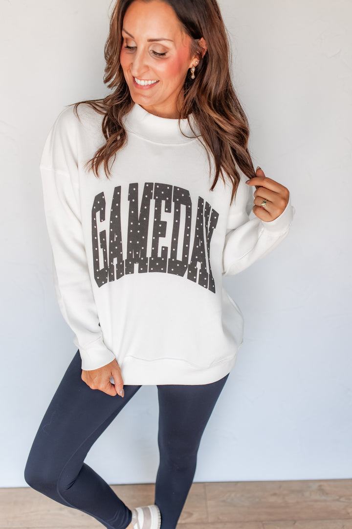 Woman wearing white polka dot GAMEDAY mockneck sweatshirt with black leggings