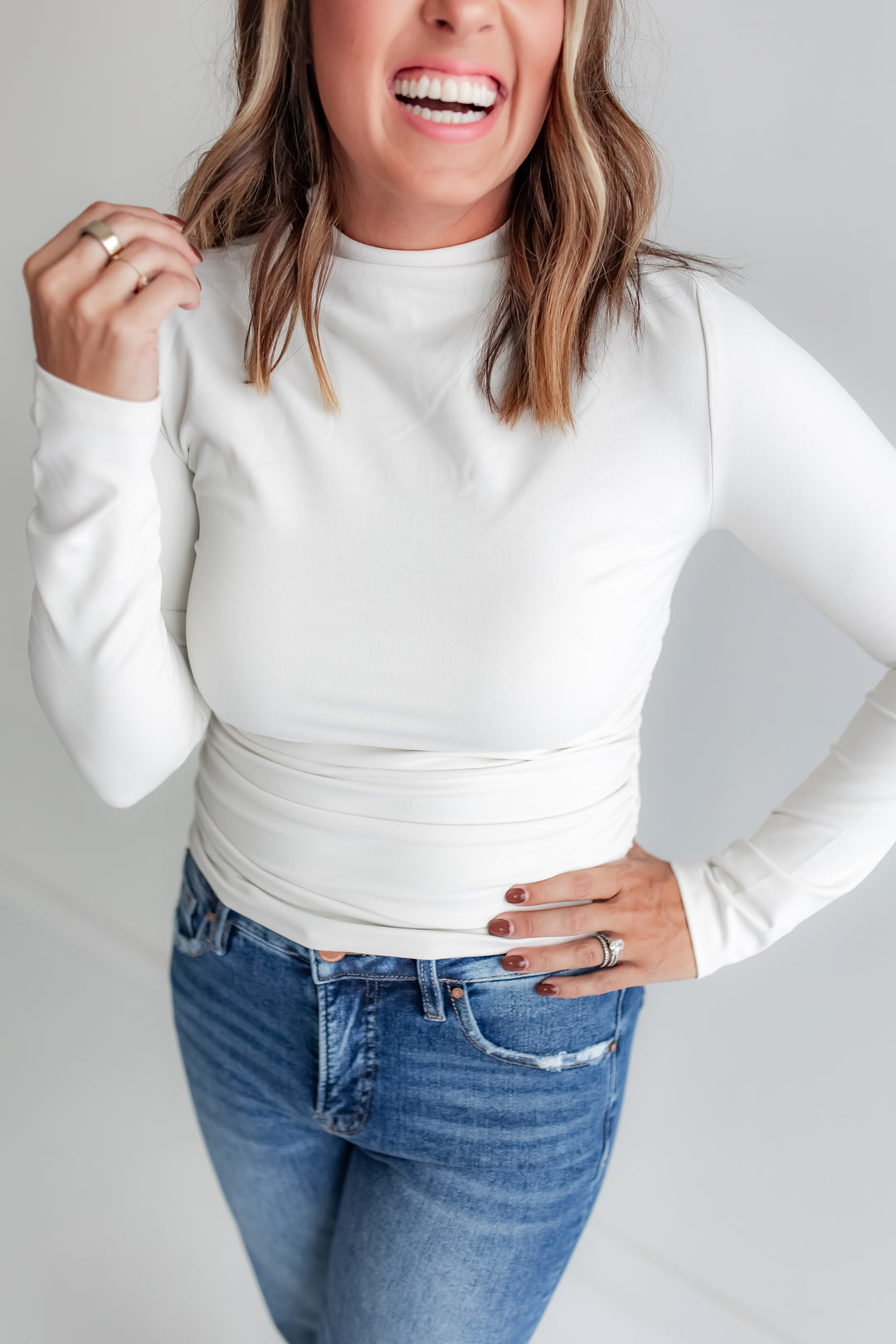 Woman wearing a white long-sleeve top and blue jeans against a plain background