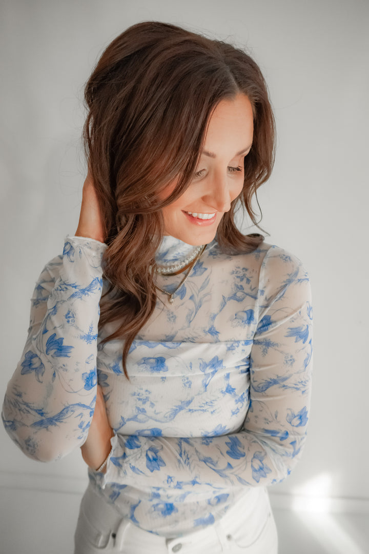Woman wearing a light blue floral bodysuit against a plain background