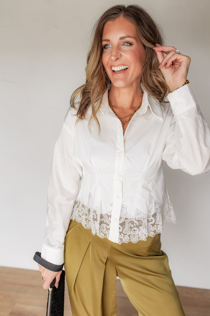 Woman wearing white poplin button-up blouse with sheer lace hem trim, styled with olive satin pants