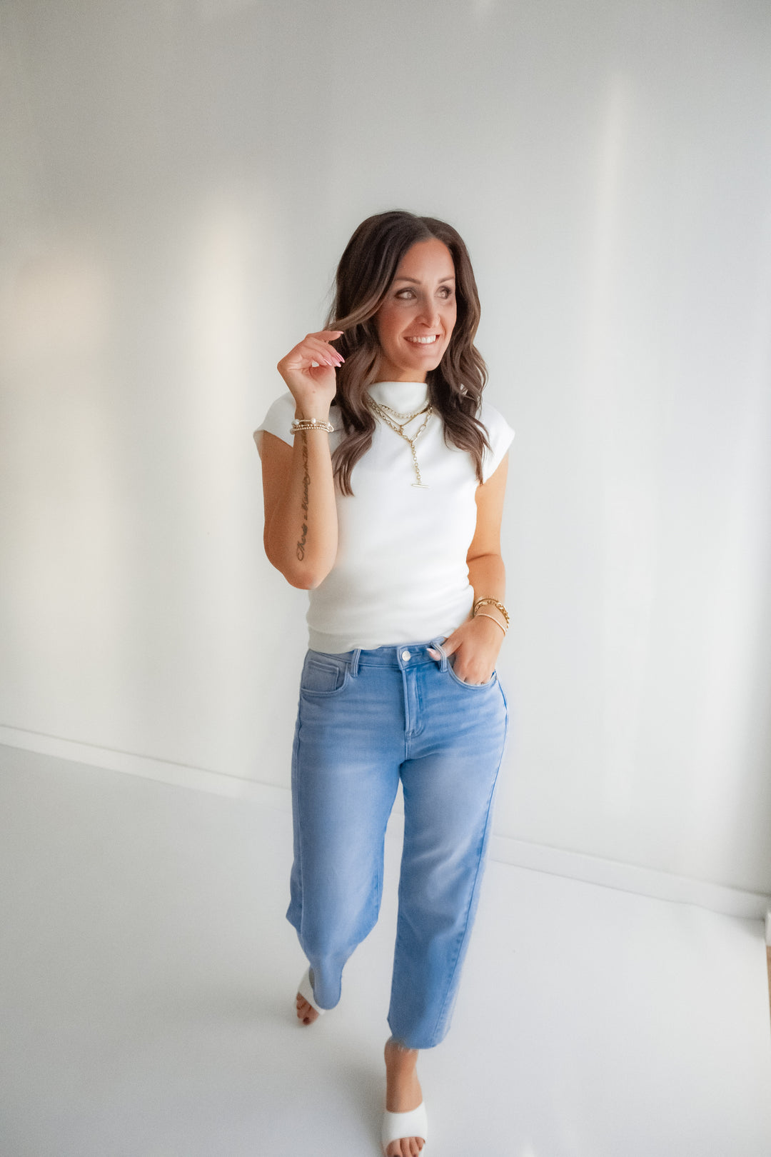 Woman wearing a white top and blue jeans against a plain white wall
