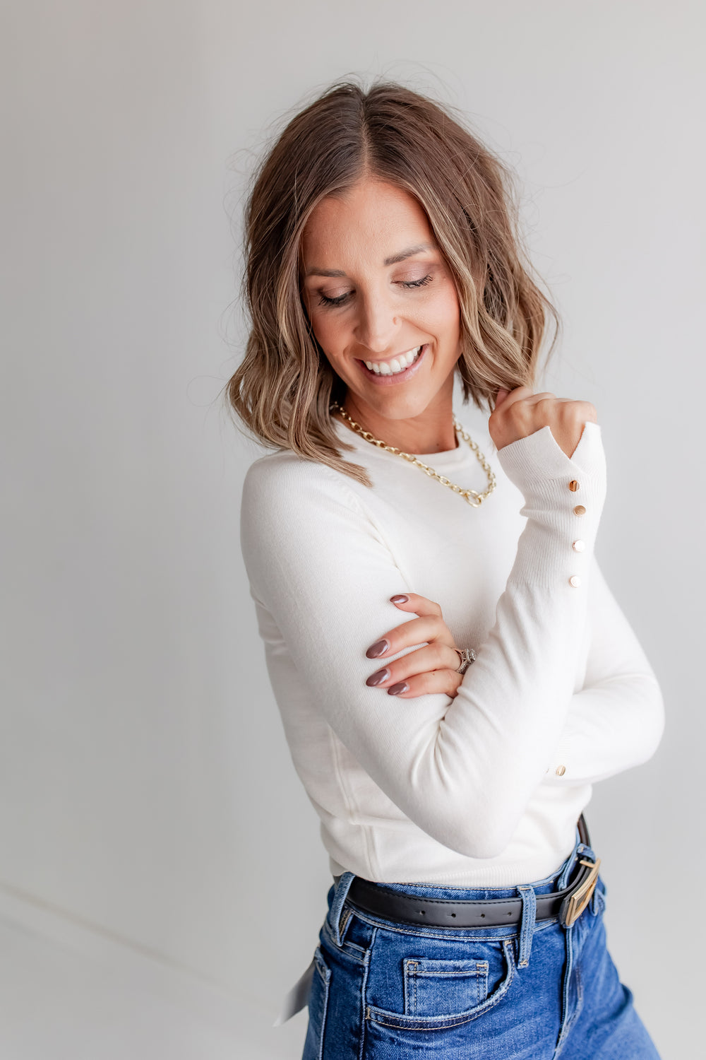 Model wearing ivory blouse with gold button detail at the cuff. 