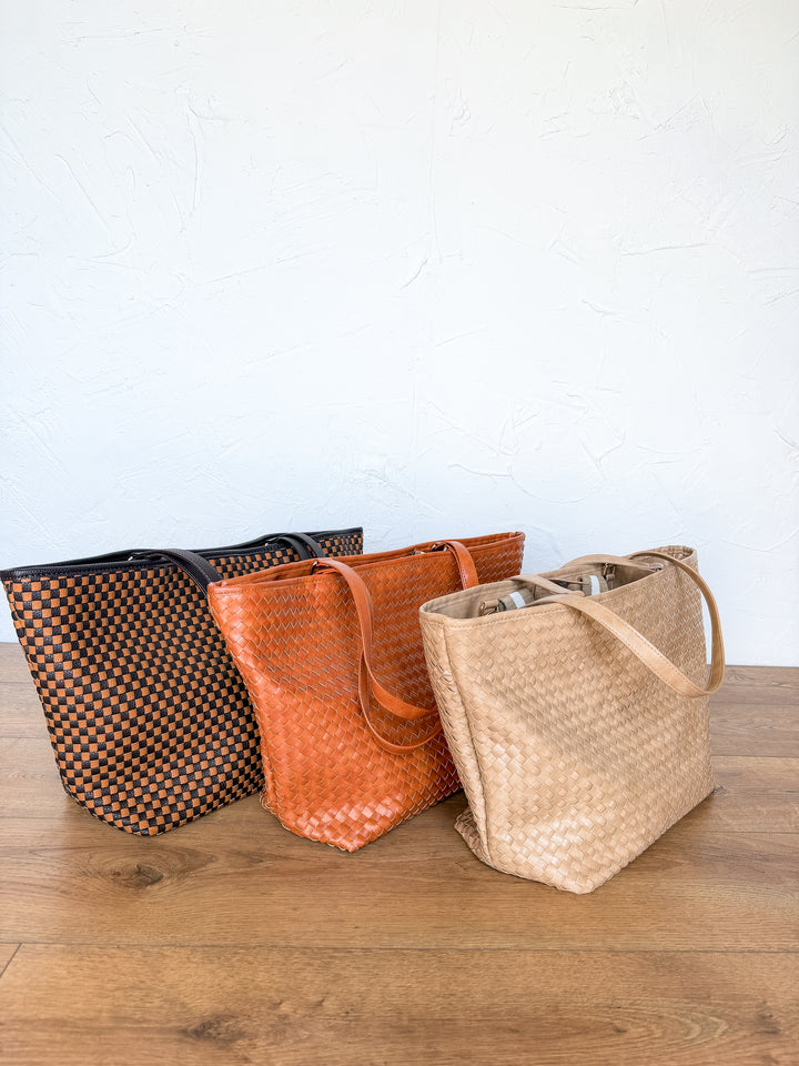 Three woven tote bags in black checkerboard, cognac, and tan side by side