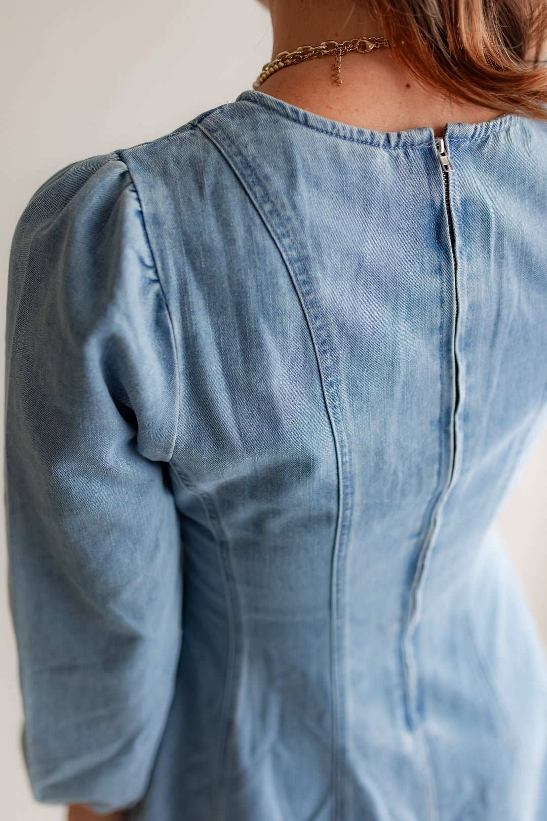 close up of a light wash denim dress with long sleeves and zipper on the back. 